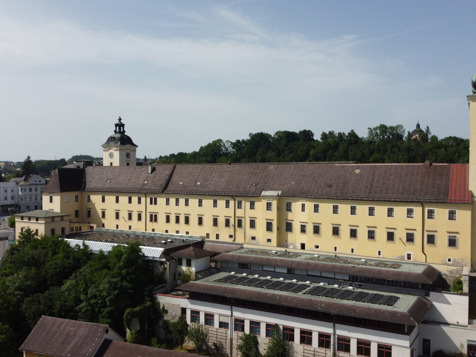 DCIM100MEDIADJI_0162.JPG Ein großes, gelbes historisches Gebäude mit Türmen und rotem Dach, umgeben von Bäumen und Straßen unter einem klaren Himmel.