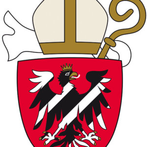 Das Wappen zeigt einen gekrönten schwarzen Adler mit weißen Markierungen auf einem roten Schild, über dem eine Bischofsmitra, ein Bischofsstab und ein weißes Objekt hinter dem Schild abgebildet sind.